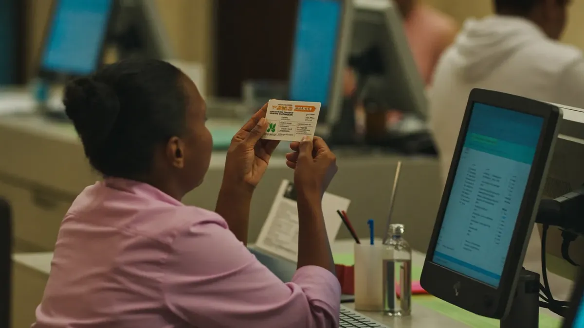 An adult patient at a Colorado urgent care clinic reception desk with an insurance card, staff behind glass