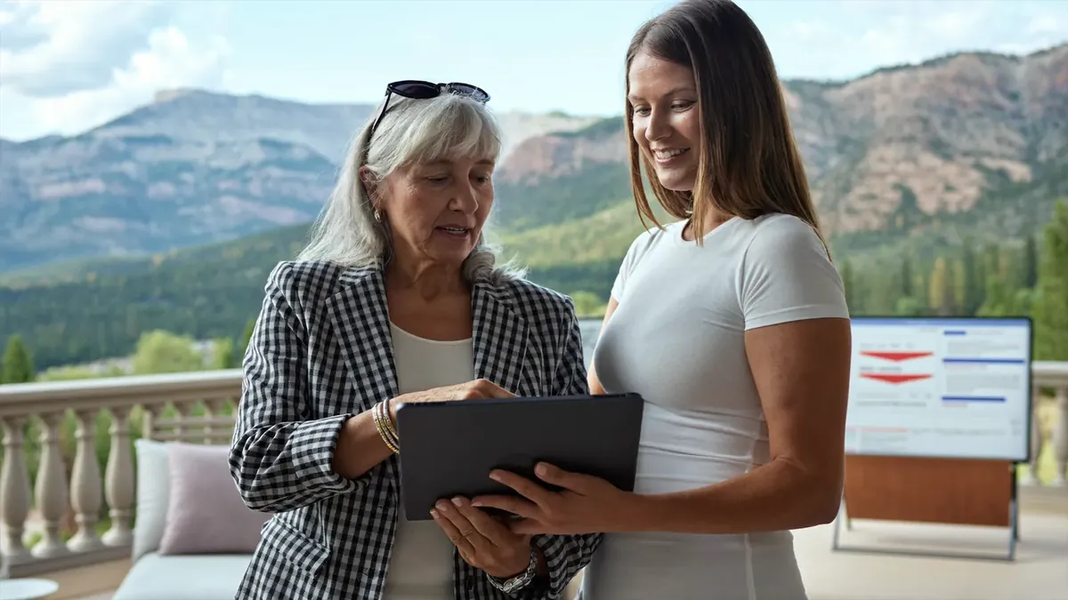 An older woman and a young female insurance representative looking at a tablet with plan details in a sunlit living room