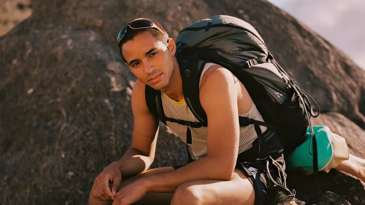 A young adult rock climber resting at a Colorado crag, healthy and active, backpack beside him