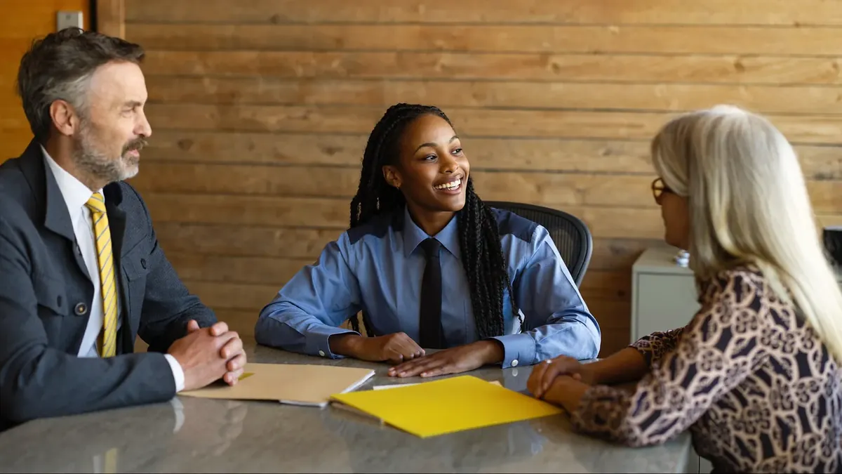 A young insurance representative showing two plan comparison sheets side by side to an older couple across a desk