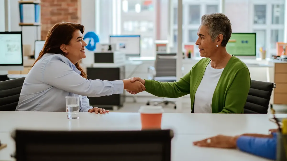 A young insurance broker shaking hands with an older client in a bright Broomfield, Colorado office