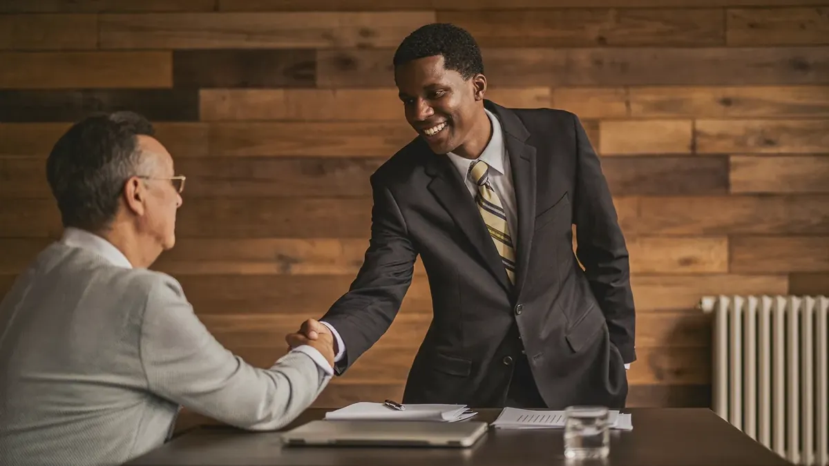 A young insurance broker shaking hands with an older client in a bright Broomfield, Colorado office