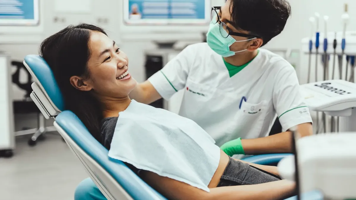 A smiling older adult in a bright modern Colorado dental office chair talking with a young dentist