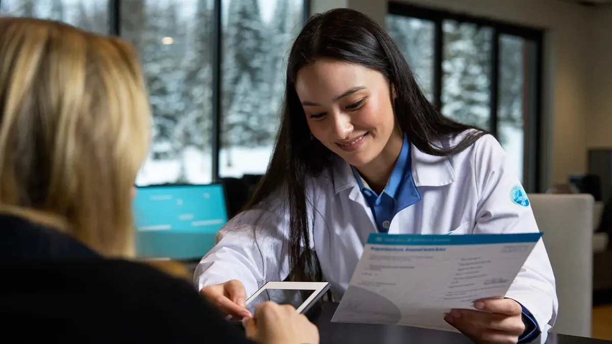 A friendly young insurance advisor helping an adult client choose a health plan in a sunny Colorado office