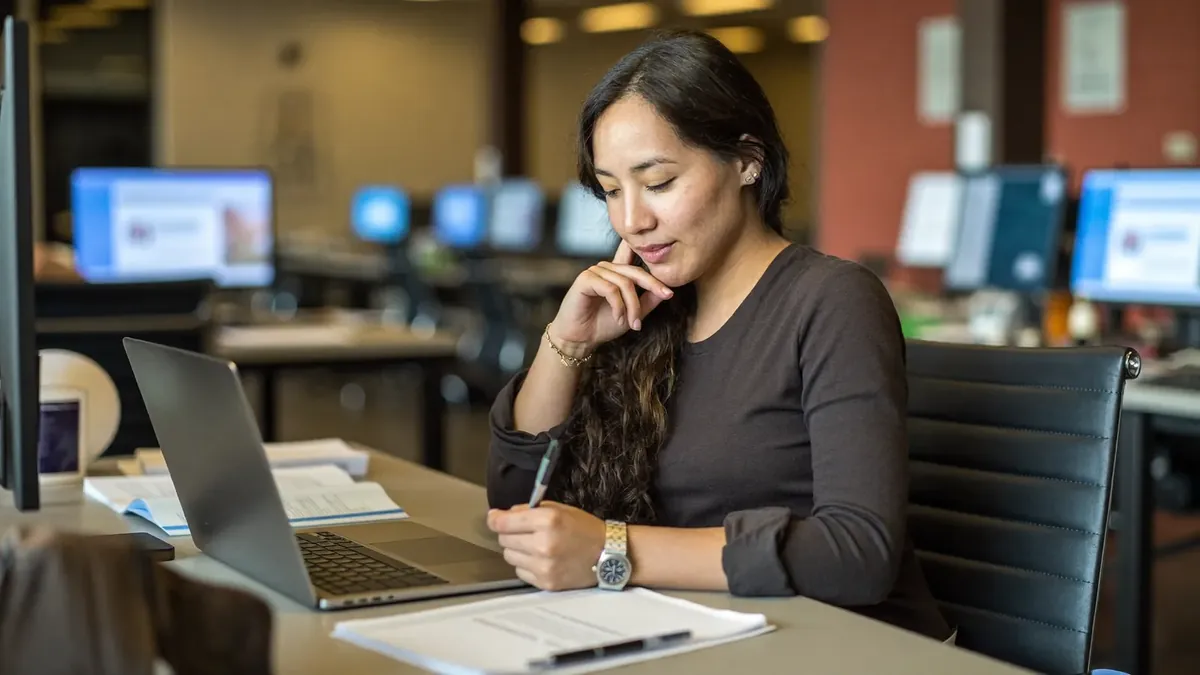 A young insurance professional studying licensing materials at a desk in a Denver co-working space, laptop and notes