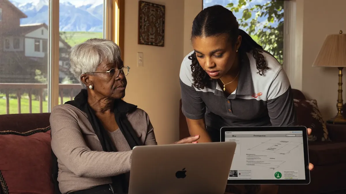 An older woman and a young female insurance representative looking at a tablet with plan details in a sunlit living room