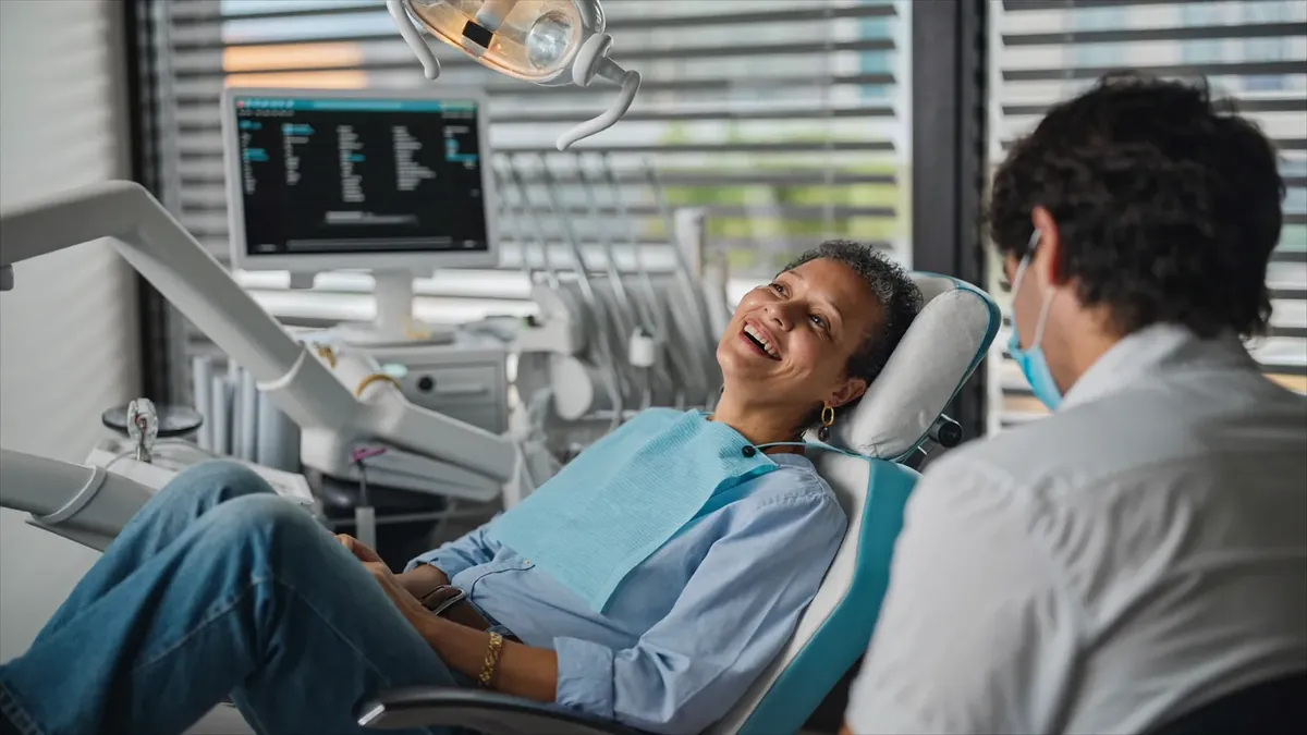 A smiling older adult in a bright modern Colorado dental office chair talking with a young dentist