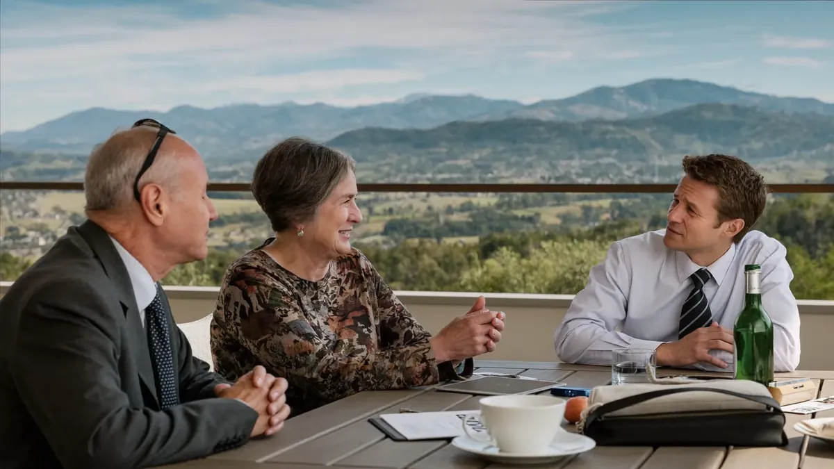 A senior couple and a young insurance broker sitting together at a table in a Colorado office, mountain view window